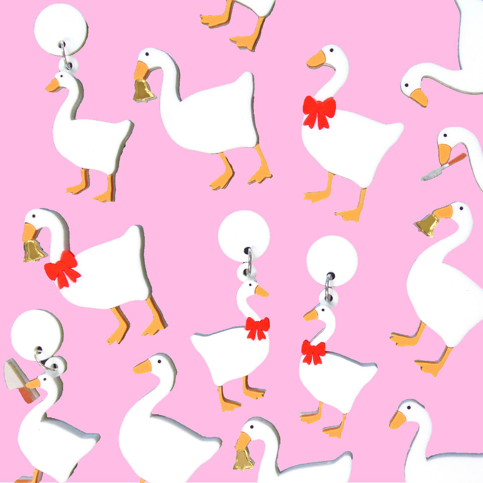 Goose brooches and earrings. All the geese are white, with orange feet and beaks. Some are holding gold coloured bells, others have red bows around their necks, some are wielding silver coloured butter knives, others are plain and some have bows and bells