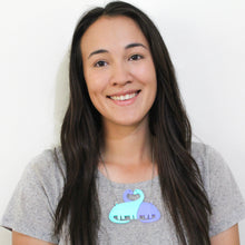 Load image into Gallery viewer, Portrait of a half-asian woman with long dark brown hair in a middle part in a grey t-shirt wearing a dinosaur necklace. The necklace is of two brontosaurus; one mint green, one purple, hanging from a fine metal chain.
