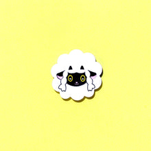 Load image into Gallery viewer, A sheep brooch in front of a yellow background. The sheep is like a fluffy cloud, with a black face and ears popping out and two small little horns.
