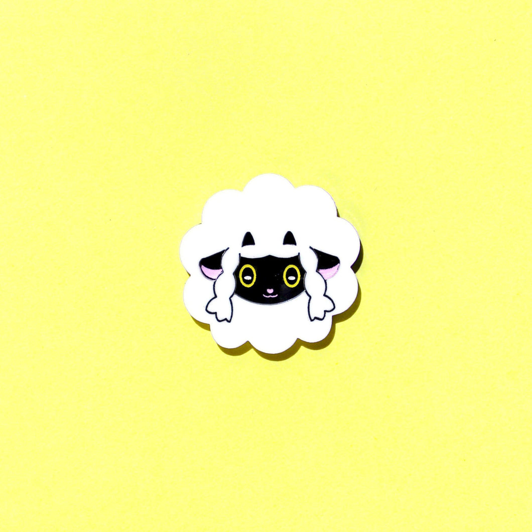 A sheep brooch in front of a yellow background. The sheep is like a fluffy cloud, with a black face and ears popping out and two small little horns.