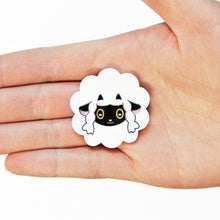 Load image into Gallery viewer, A close up of a sheep brooch in a hand facing up. The sheep is cartoonish with a circular, fluffy body like a cloud and large oval eyes, a small pink nose and mouth, and little black horns.
