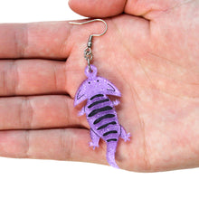 Load image into Gallery viewer, A close up of a Diplocaulus earring, an animal which is an extinct amphibian that looks like a salamander with a boomerang shaped head. The earring is made from acrylic, a type of plastic, that is light purple with silver glitter and hand painted details including black stripes along its back. The earring is hanging from a silver-coloured stainless steel hook. It&#39;s in a hand facing up in front of a white background.
