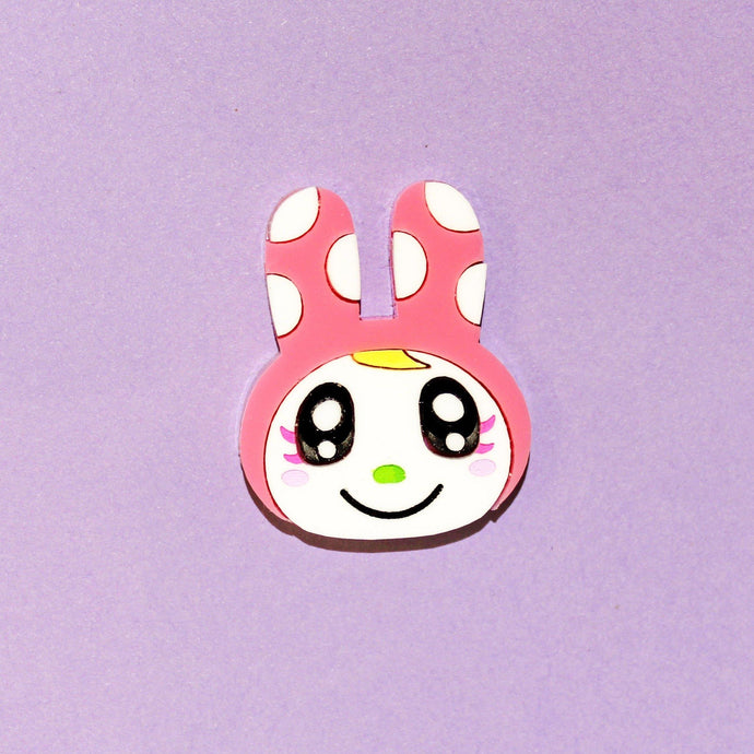 Cute Chrissy! An acrylic plastic brooch of a cartoon rabbit with green nose, black anime style eyes, hot pink eyelashes, blushing cheeks and a tuft of blond hair hiding from a pink bonnet with white polka dots.