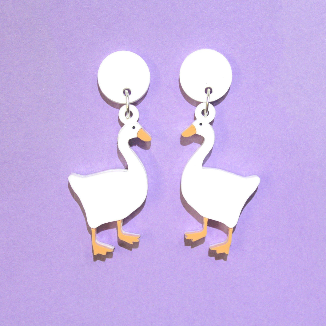 A pair of white goose earrings on a purple background.