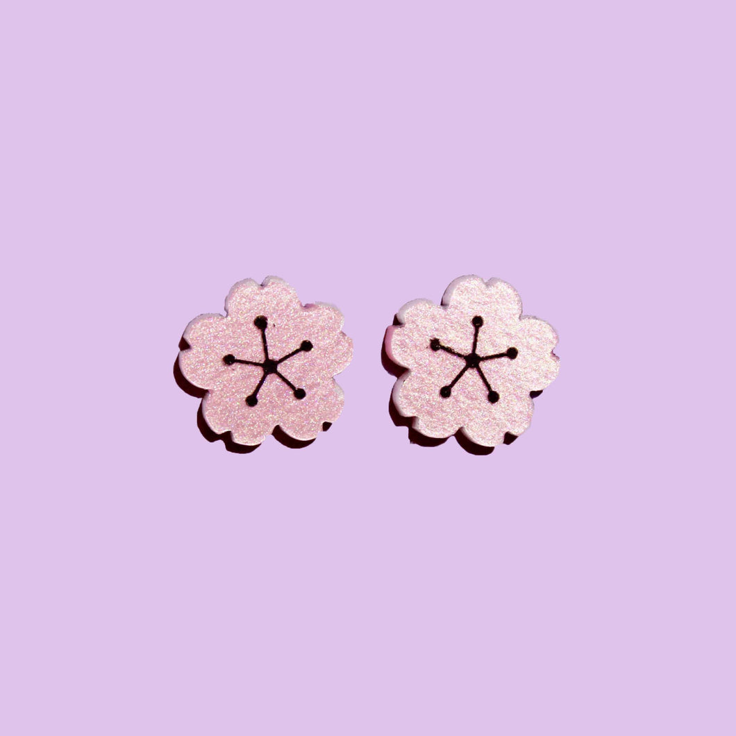 A pair of cute flower shaped earrings made from shimmery pale pink acrylic with a light purple background behind them.