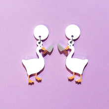 Load image into Gallery viewer, A pair of plastic earrings featuring geese holding large knives. The geese are white and mirror images, with orange bills and webbed feet on a purple background.
