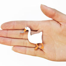 Load image into Gallery viewer, A hand hovering over a white background holding a plastic brooch of a goose holding a small knife in its beak.
