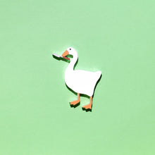 Load image into Gallery viewer, A plastic brooch of a cute looking goose holding a small butter knife in its mouth. The goose is surrounded by a green background.
