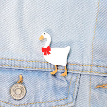 Load image into Gallery viewer, Close up of a brooch on a pale blue denim jacket. The brooch is made of a type of plastic, featuring a white goose with orange feed and beak with a red bow around its neck.
