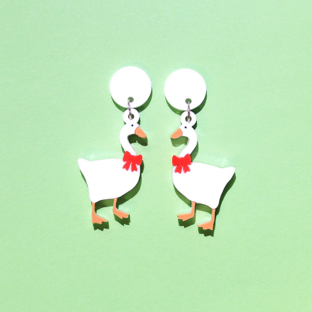 Cute earrings featuring a white goose with a red bow wrapped around its neck. The untitled goose earrings are on a pastel green background.
