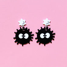 Load image into Gallery viewer, A pair of acrylic earrings in front of a pink background. The earrings are of soot sprites, black balls with big white, painted eyes and little hairs, hanging from white stars.
