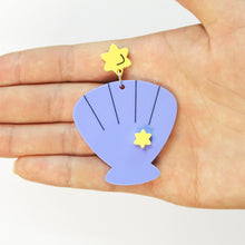 Load image into Gallery viewer, A statement earring on a hand facing palm up with a white background. The earring is made of two parts: a small yellow star at the top and a bluey purple scallop shell hanging below it.
