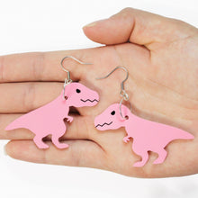 Load image into Gallery viewer, A cropped image of a hand holding two dinosaur earrings facing palm up. The dinosaurs are cartoon T rex in pink, hanging from metal earring hooks.
