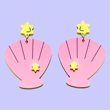Load image into Gallery viewer, A pair of pink shell earrings with a lilac background. Each earring is made of two parts: a small yellow star on top and a pink scallop shell hanging from a ring below it.
