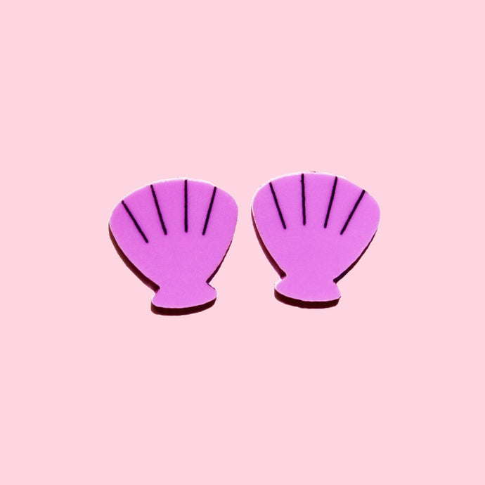 A pair of purple, scallop shell stud earrings with a pale pink background behind them.