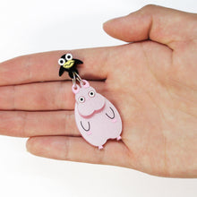 Load image into Gallery viewer, A close up of an earring made of two parts: a black bird attached to a large pink mouse by two silver coloured rings. The earring lies on a hand, facing up over a white backdrop.
