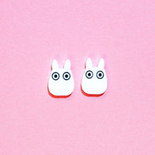 Load image into Gallery viewer, A cute pair of earrings resembling two white rabbits with large cartoon eyes in front of a pink background.
