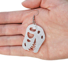 Load image into Gallery viewer, A close up of a T rex skull earring on a hand. The earring is kind of large, about 5cm long and 3cm wide and hanging from a silvertone stainless steel hook. The earring is held in the palm of a young woman in front of a white background.
