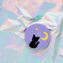 Load image into Gallery viewer, A cat brooch in front of a shiny, holographic background. The brooch is 5cm and circular, with a pastel purple background, pastel yellow crescent moon and stars at the top and a black cat sitting at the bottom. 
