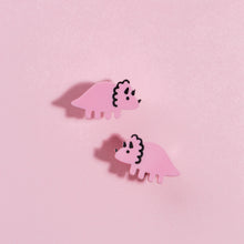 Load image into Gallery viewer, A cute pair of sweet little Triceratops stud earrings in pink with black details. A Triceratops is a type of herbivore that walks on all fours, with a tail and three horns and a frill around its neck. The eyes, horns and frill of these Triceratops earrings are hand painted in black. The earrings are small studs, made from acrylic, a type of plastic, with stainless steel posts. The earrings are in front of a baby pink background.
